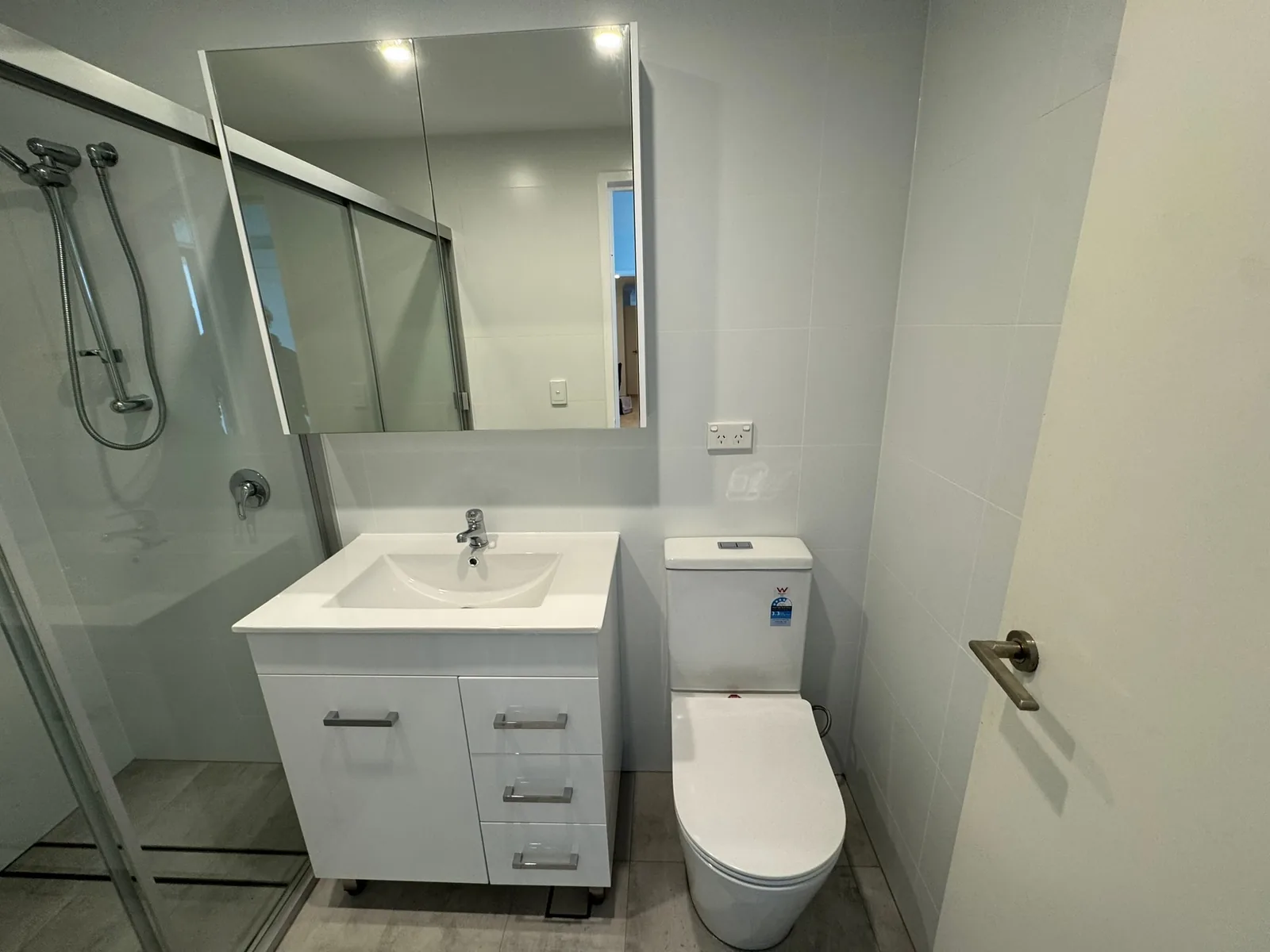 Compact bathroom renovation with a white vanity, mirrored cabinet and shower screen