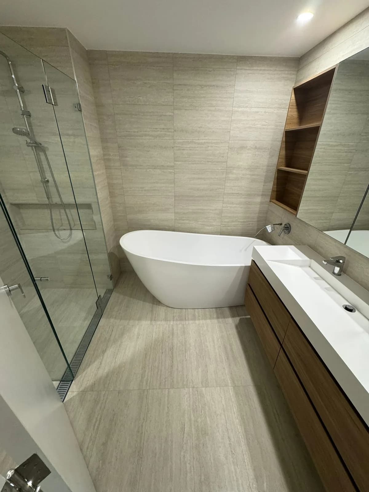 Ensuite with a freestanding bath, frameless glass shower and travertine-look tiling