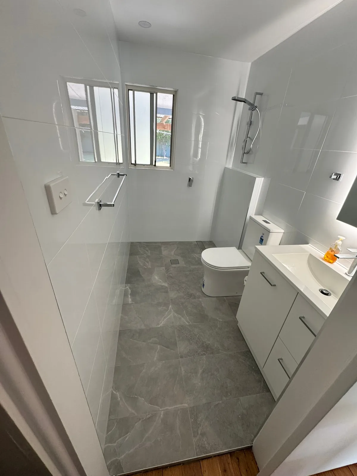 Renovated bathroom with white wall tiles, grey marble-look floor tiles and a walk-in shower