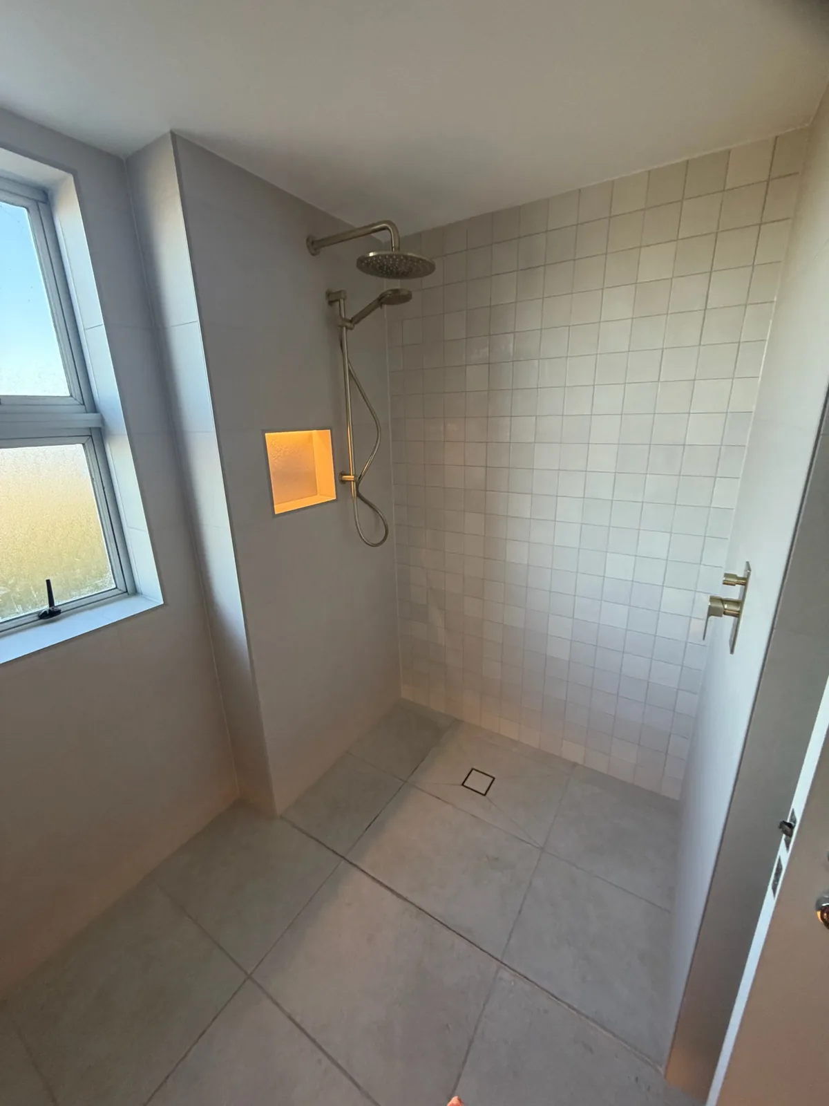 Shower with a lit recessed niche, tiled walls and a window above
