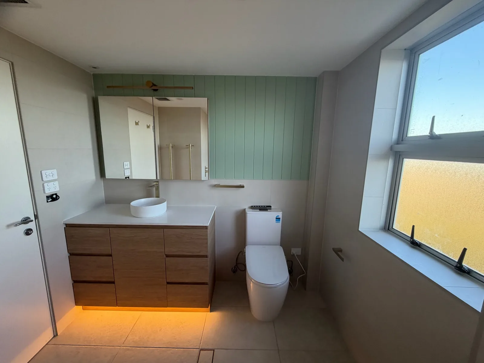 Renovated bathroom with a custom timber vanity, stone benchtop, sage green panelling and under-cabinet lighting
