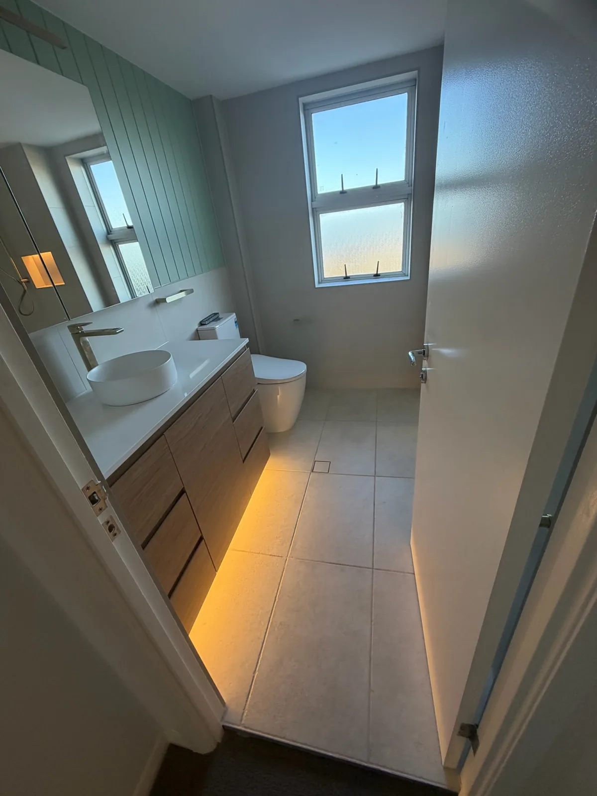 Bathroom vanity with a stone benchtop and warm LED strip lighting under the cabinet