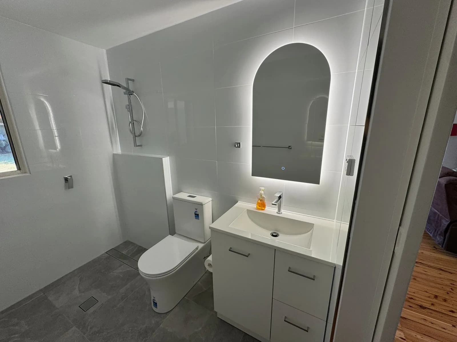 Bathroom vanity with an arched mirror and white cabinetry beside a toilet