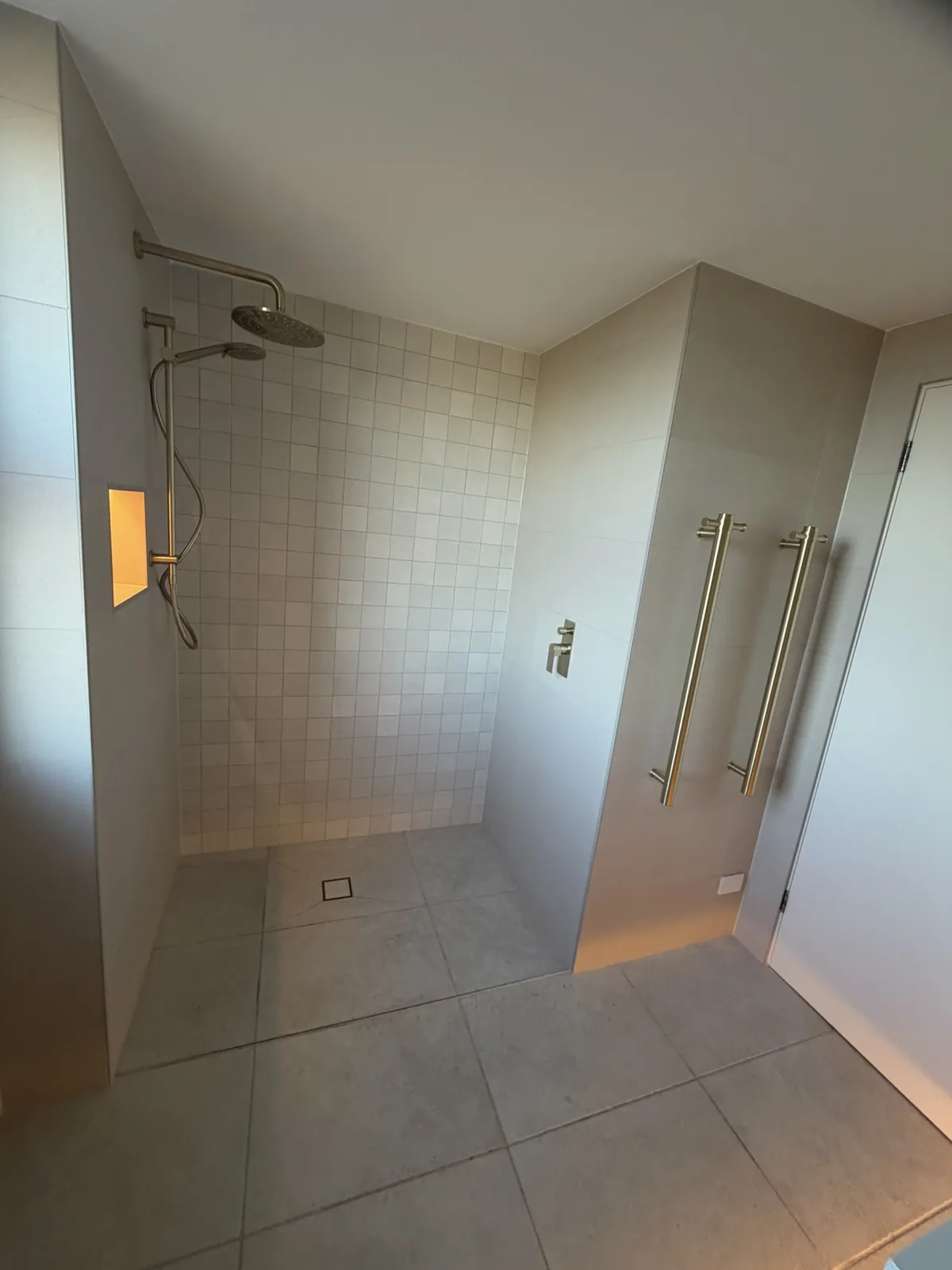Tiled walk-in shower with a brushed brass rain head, lit niche and heated towel rails