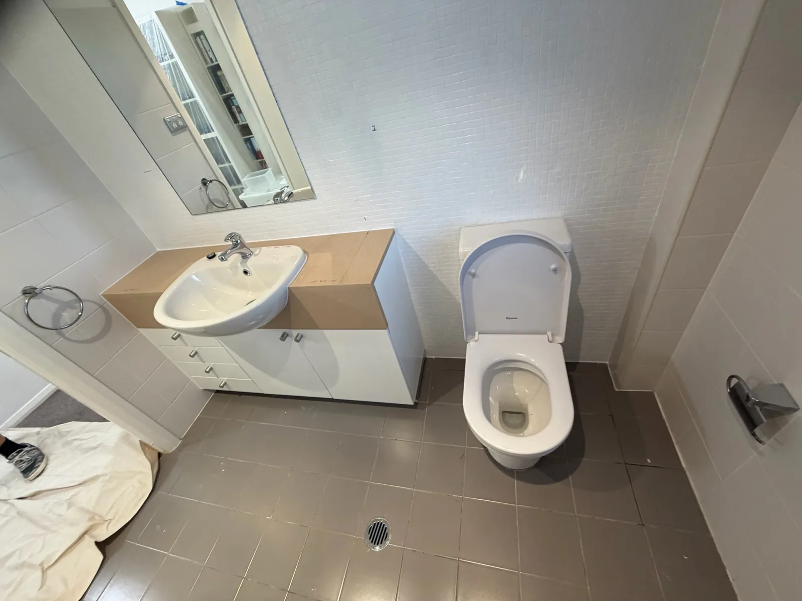 Dated apartment bathroom before renovation, with a laminate vanity top and brown floor tiles