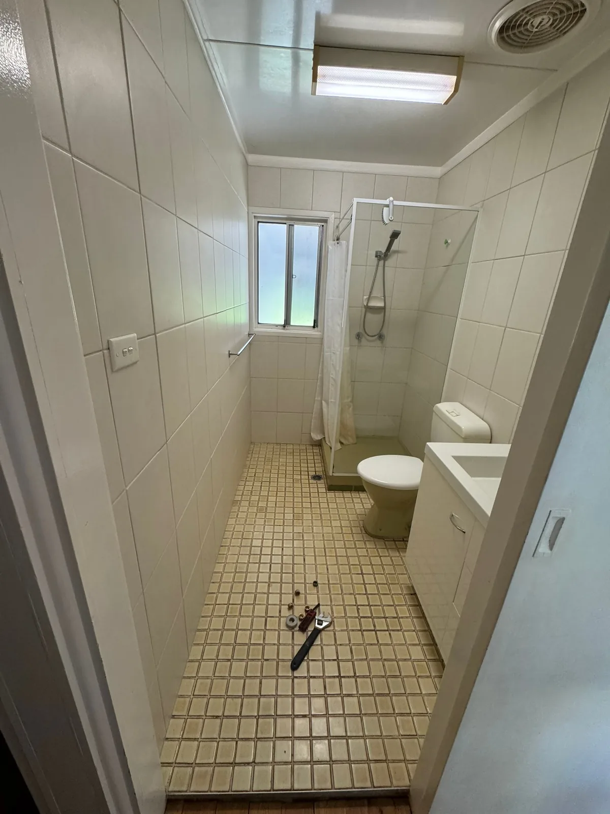Original bathroom before renovation, with dated wall tiles and a small mosaic tile floor