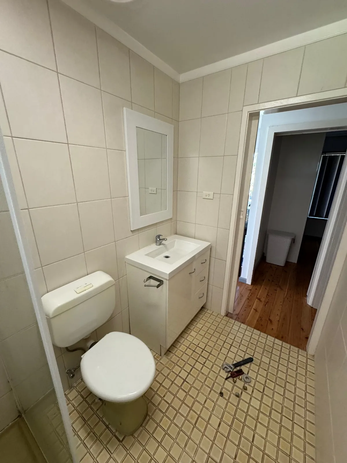 Original bathroom before renovation, with a small vanity and worn floor tiles