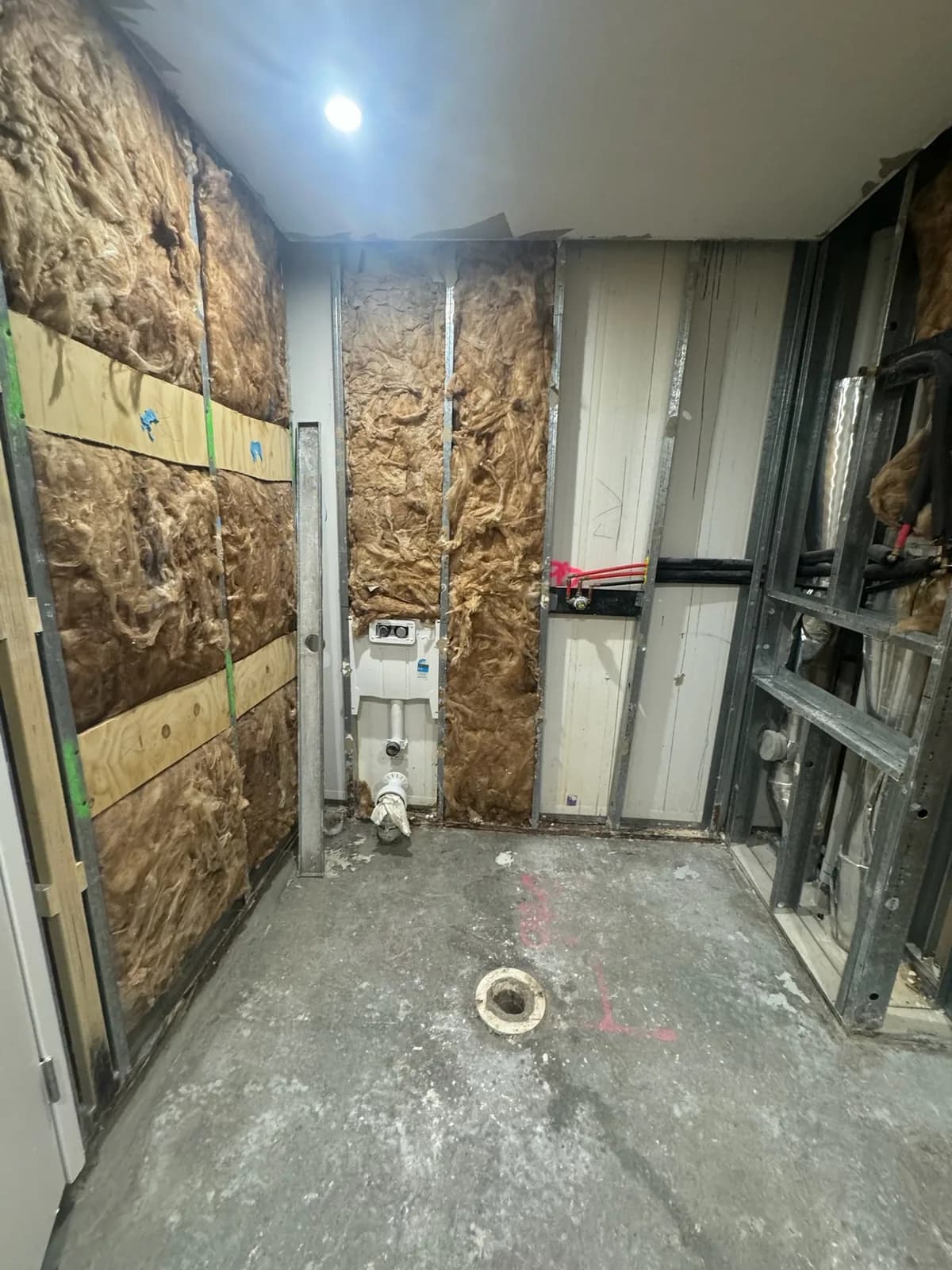 Steel stud framing with insulation batts and a wall-hung toilet cistern set into the wall