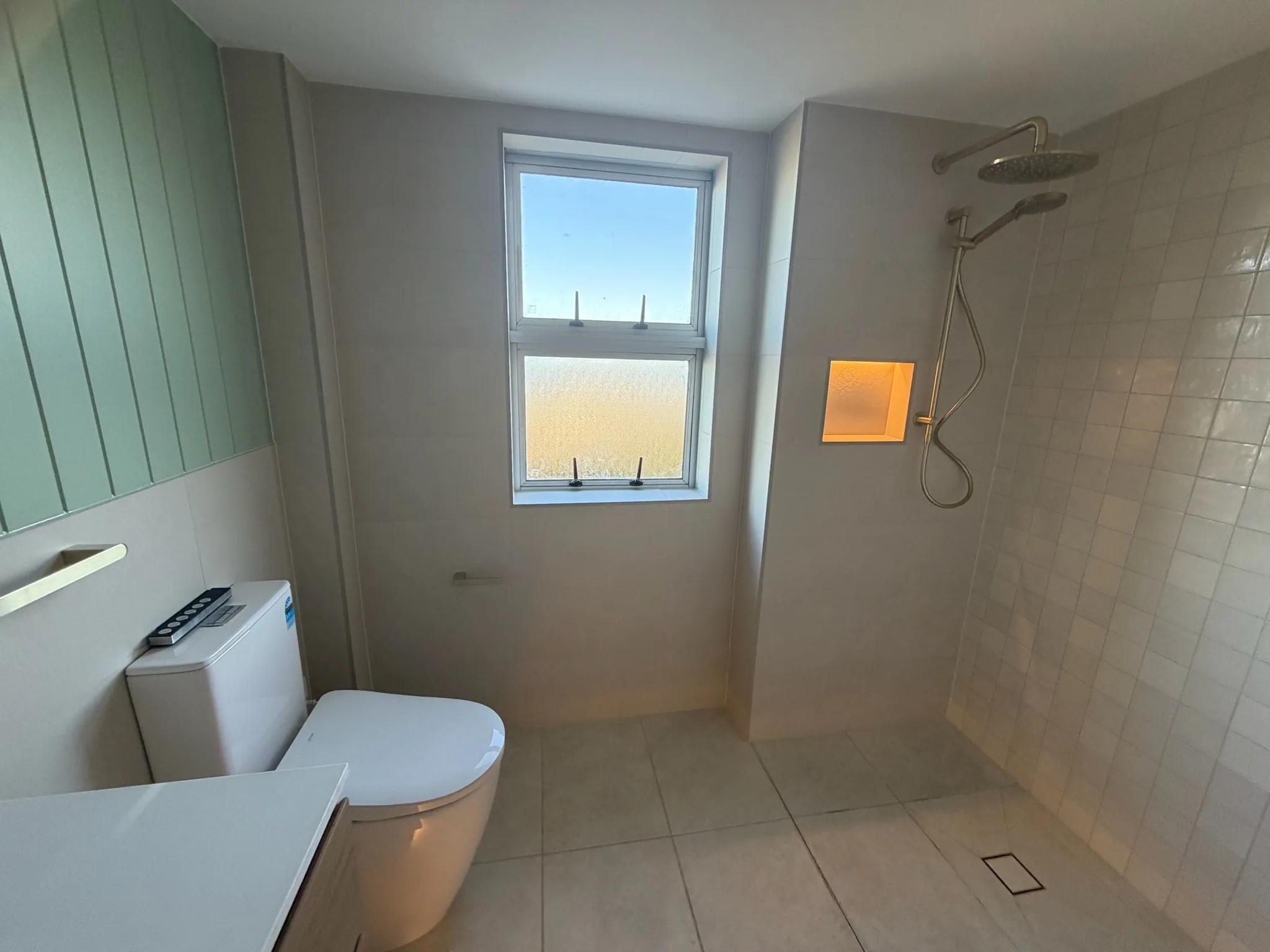 Completed bathroom renovation with a tiled walk-in shower, brushed brass rain head and a lit wall niche