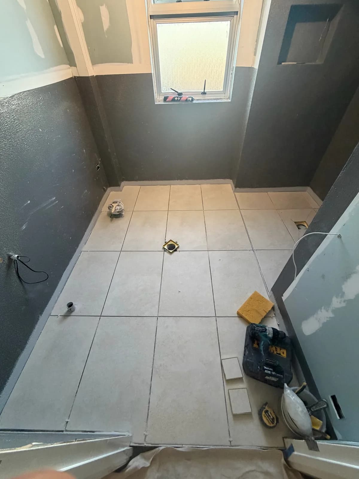 Large-format floor tiles laid out and levelled across a bathroom floor