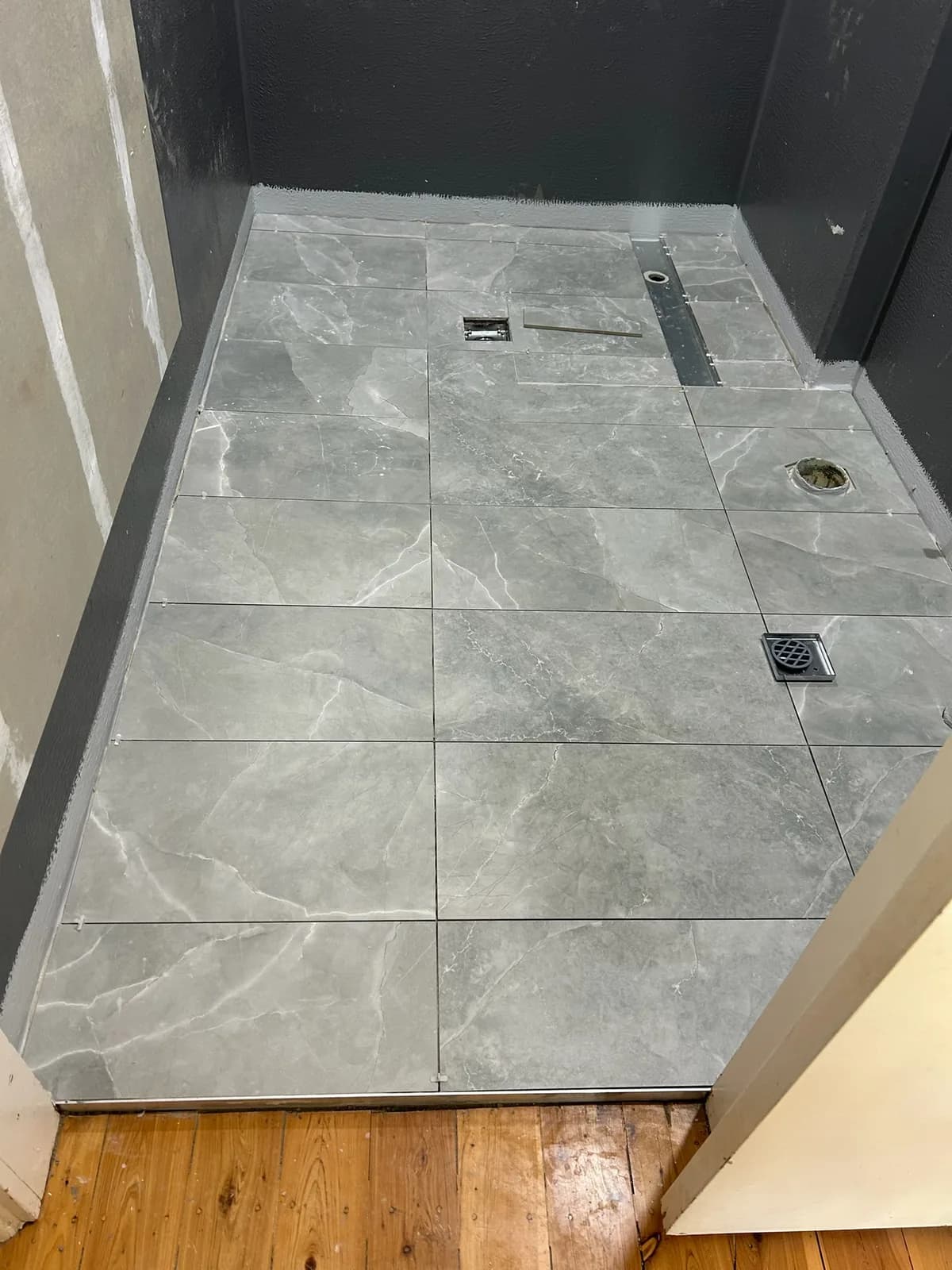 Grey stone-look floor tiles laid with a linear drain and floor waste set flush