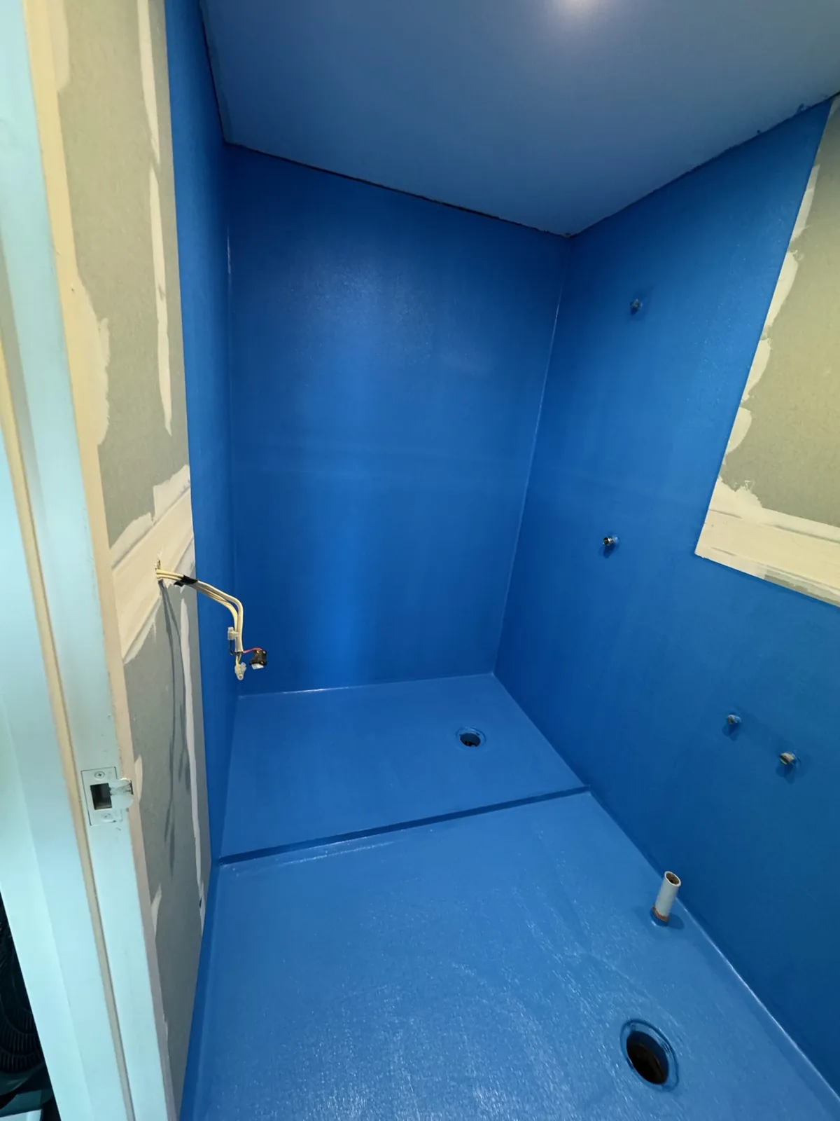 Blue waterproofing membrane applied to shower walls and floor, coved into the corners
