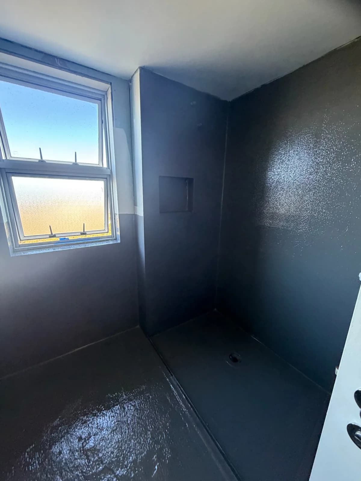 Charcoal waterproofing membrane coved up the wall corners beneath a window