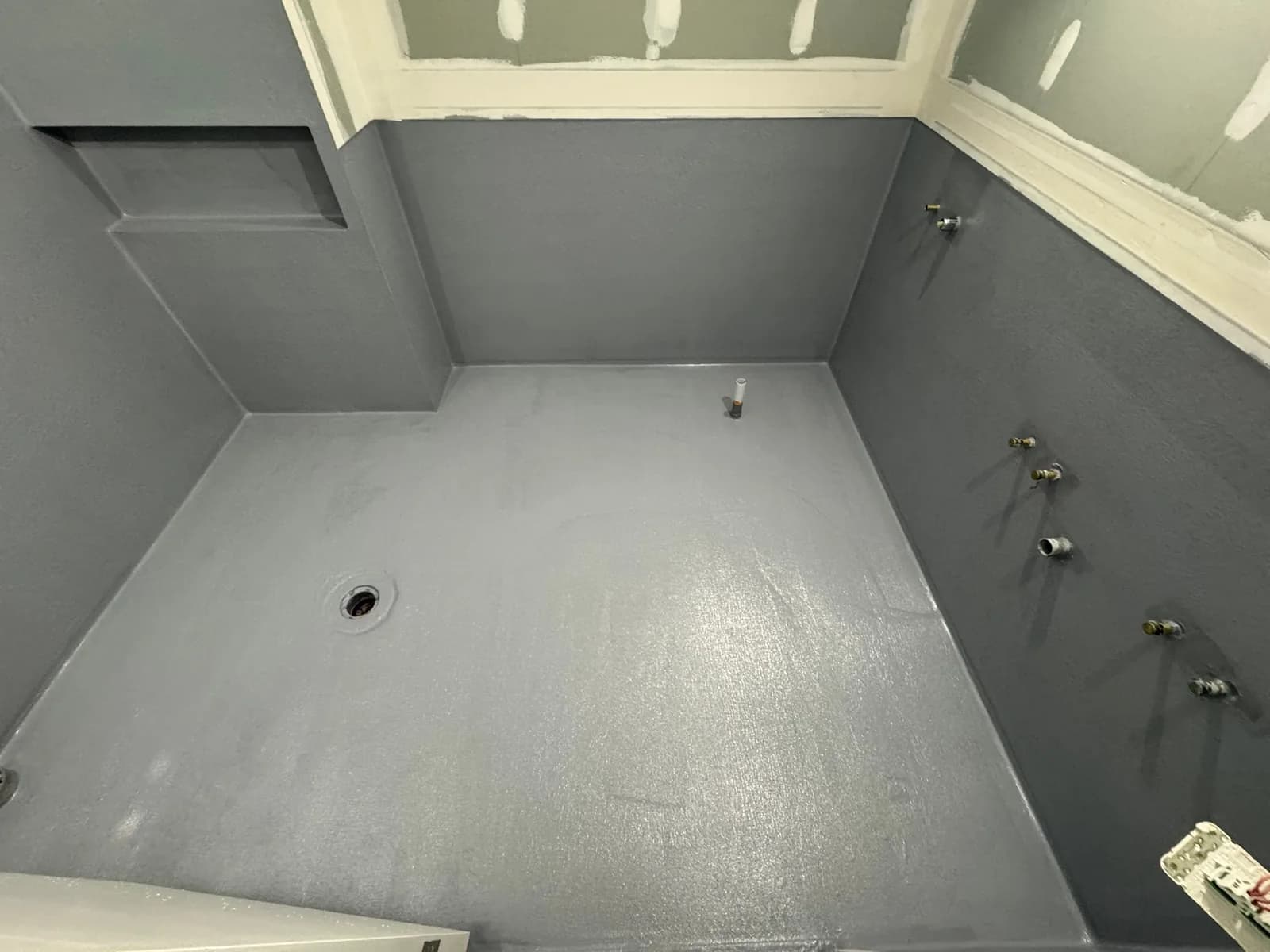 Waterproofing membrane rolled over a bathroom floor and coved up the wall junctions