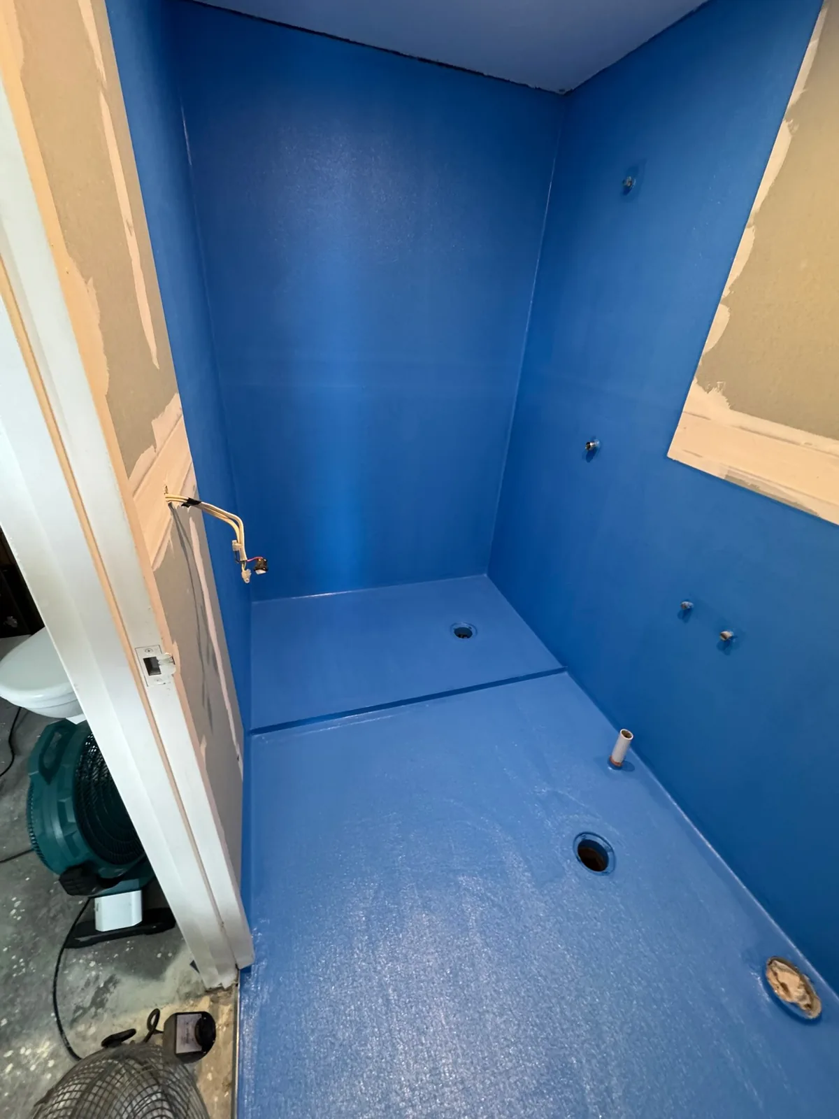 Shower recess coated in blue waterproofing membrane before tiling, with the floor waste set in